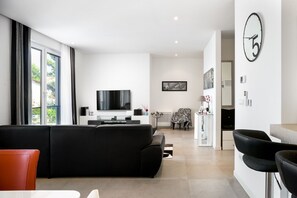 A modern living room with a black sofa, a flat-screen TV, and a dining area with a table and chairs.