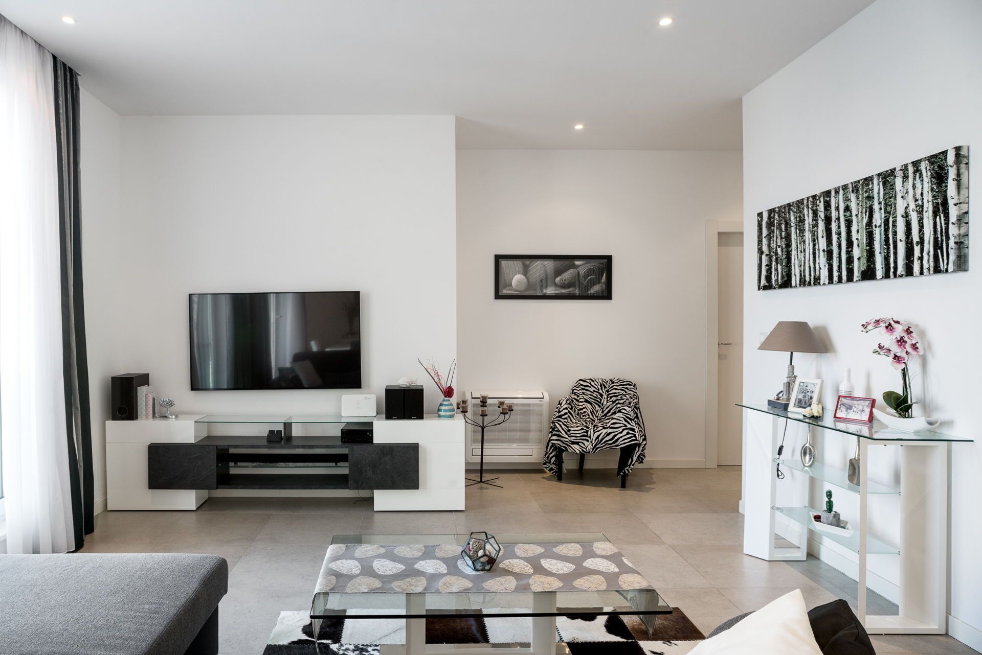 A modern living room with a flat-screen TV, a zebra-patterned chair, and a glass coffee table.