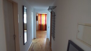 A hallway with wooden flooring, a door on the left, a mirror on the wall, and a radiator on the right. - 77qm 4Pers SatTV Garden Bed linen Towels Final cleaning Parking Washing machine  (Weissensberg)