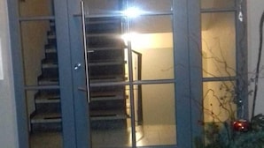 A modern entrance with a glass door, a staircase inside, and a potted plant outside. - 77qm 4Pers SatTV Garden Bed linen Towels Final cleaning Parking Washing machine  (Weissensberg)