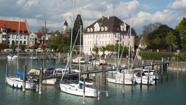 A marina with several boats docked, a large building with a red roof, and a clear sky. - 77qm 4Pers SatTV Garden Bed linen Towels Final cleaning Parking Washing machine  (Weissensberg)
