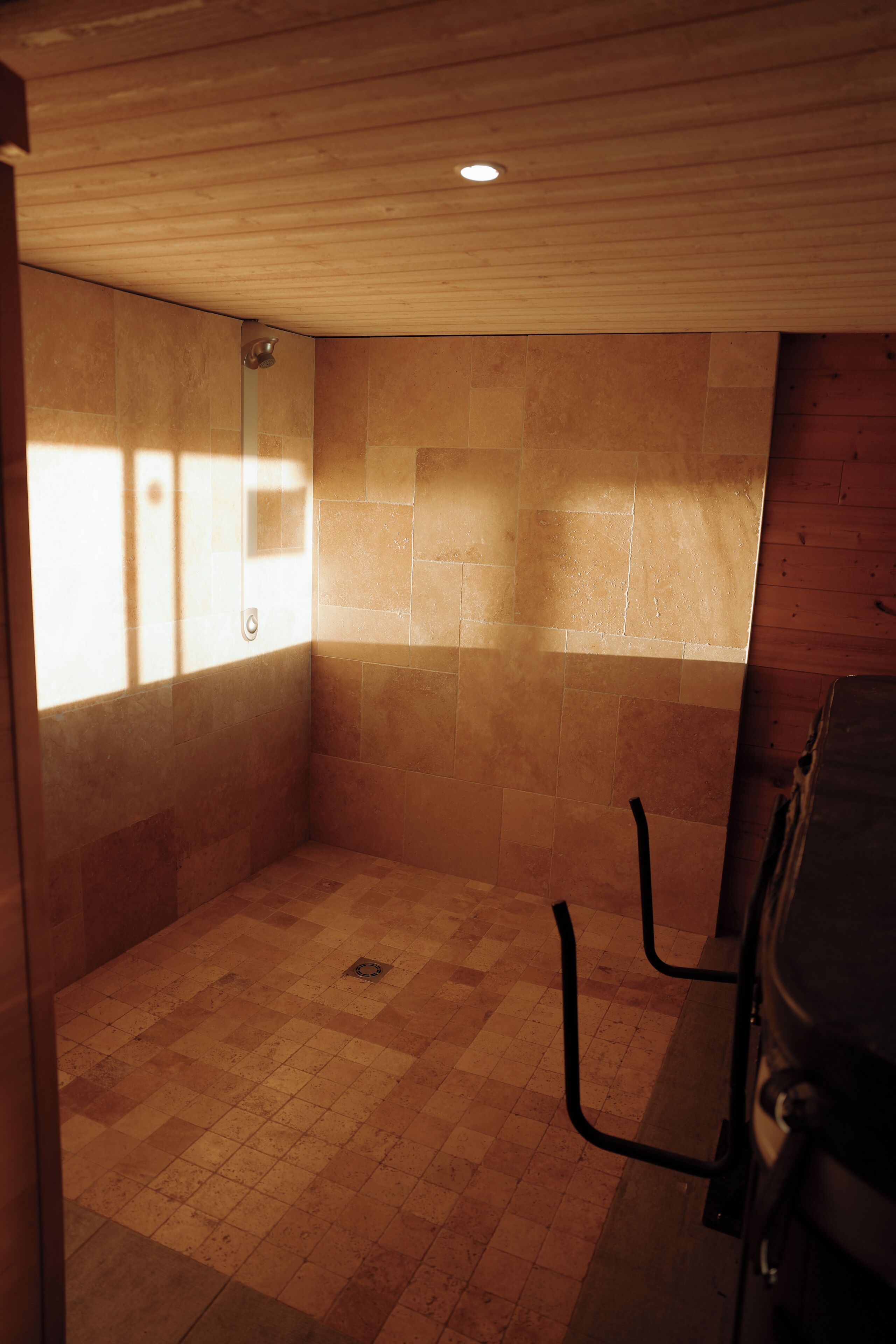 Ein Duschbereich mit gefliesten Wänden und Boden, Holzboden und einem Fenster für natürliches Licht.