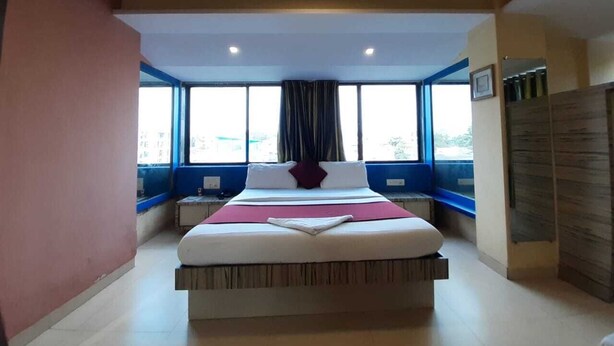 A bedroom with a large bed, a window with curtains, and a ceiling fan. - Hotel Arma (Mumbai)