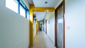 A hallway with yellow walls, a tiled floor, and a wooden door on the right. - Hotel Arma (Mumbai)