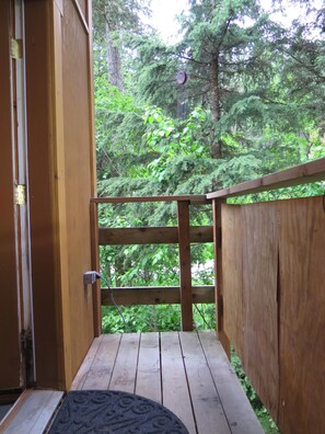 A wooden deck with a metal railing, a door, and a view of dense green foliage. - Bright, open Girdwood studio (Anchorage)