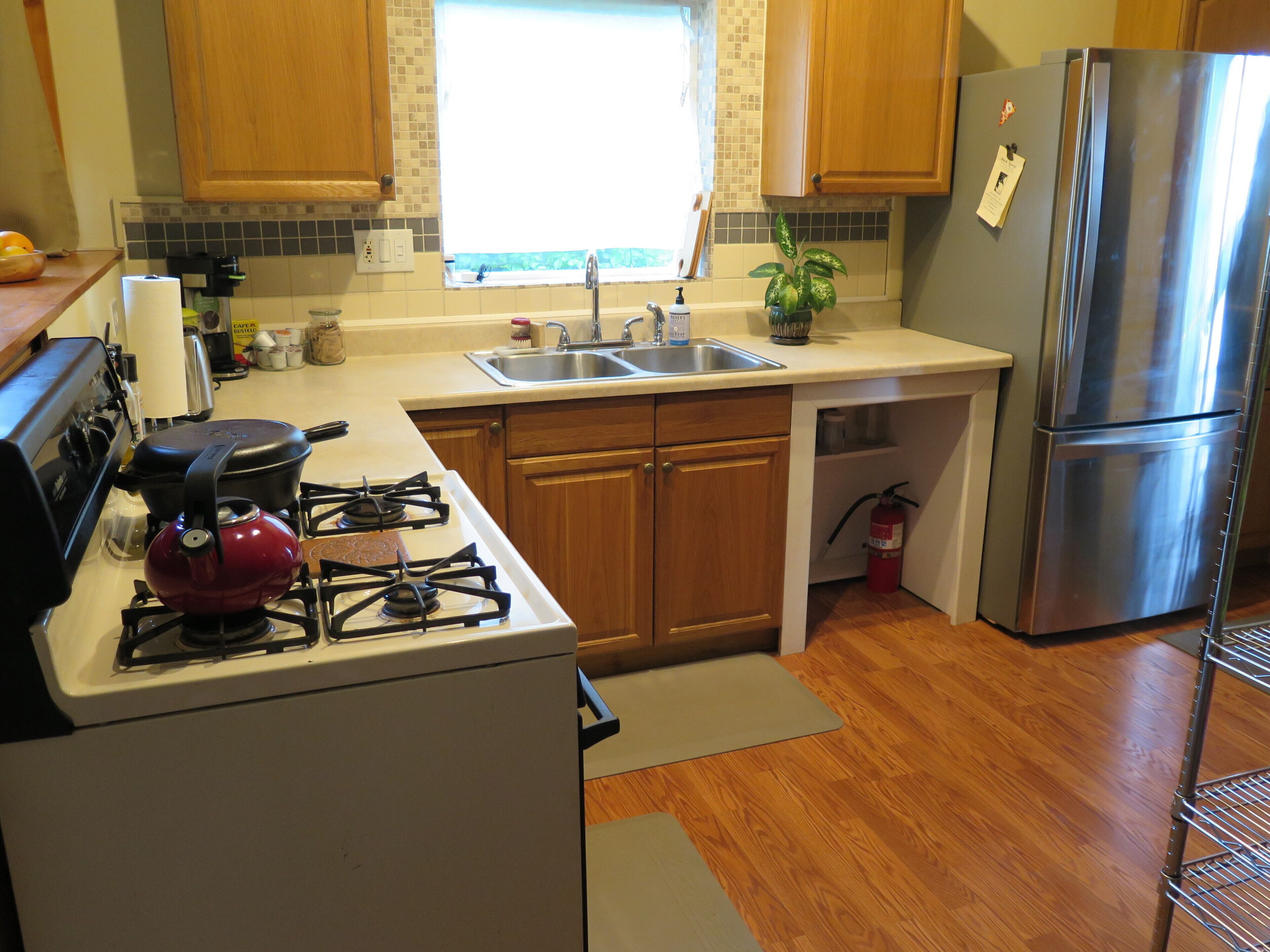 A kitchen with wooden cabinets, a stainless steel refrigerator, a gas stove, and a sink.