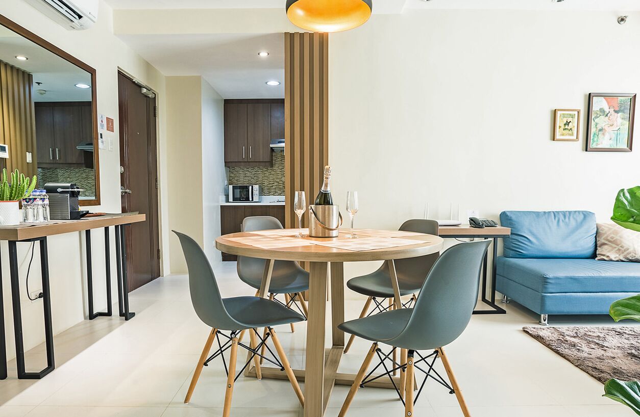 Un salon moderne avec une table de salle à manger ronde en bois, quatre chaises, un canapé bleu et une cuisine en arrière-plan.