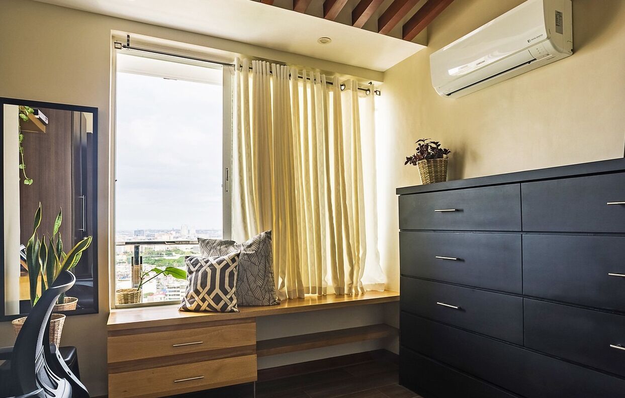 Una habitación con un ventanal grande, un aparador oscuro y un aire acondicionado de pared.