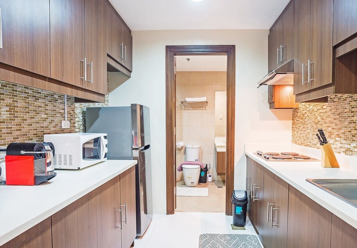 A compact kitchen with wooden cabinets, a microwave, a coffee machine, and a sink.