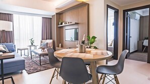 A modern living room with a dining area, a flat-screen TV, and a large window with curtains. - Padgett Place - Deluxe Suites (Cebu City)