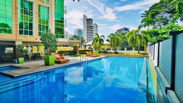 A swimming pool with lounge chairs and a modern building with large windows. - Padgett Place - Deluxe Suites (Cebu City)