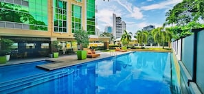 A swimming pool with lounge chairs and a modern building with large windows. - Padgett Place - Deluxe Suites (Cebu City)