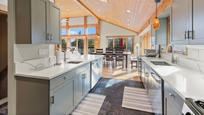 A modern kitchen with grey cabinets, a large island, and a dining area with a table and chairs. - Spectacular Peak 7 Open and Great Views! STR21-01365 (Breckenridge)