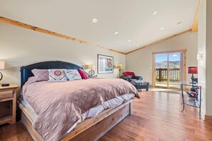 Ein Schlafzimmer mit einem großen Bett, Holzbalken, einem Fenster mit Blick und einer Tür, die auf einen Balkon führt.