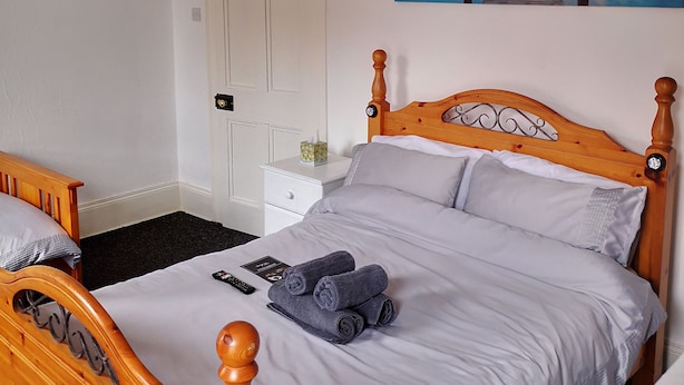 A neatly made bed with a wooden headboard, a bedside table with a lamp, and a painting of a sunset on the wall. - EuroVilla (Belfast)