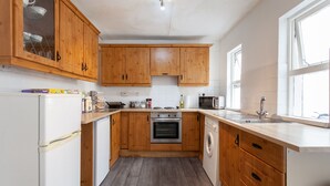 A kitchen with wooden cabinets, a microwave, an oven, a washing machine, and a sink. - EuroVilla (Belfast)