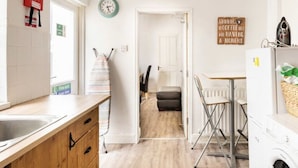 A compact kitchen with a sink, wooden cabinets, a clock, a fire extinguisher, and a laundry area. - EuroVilla (Belfast)