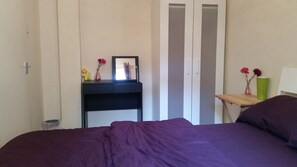 Un dormitorio con cama, un escritorio pequeño con un florero y un armario.