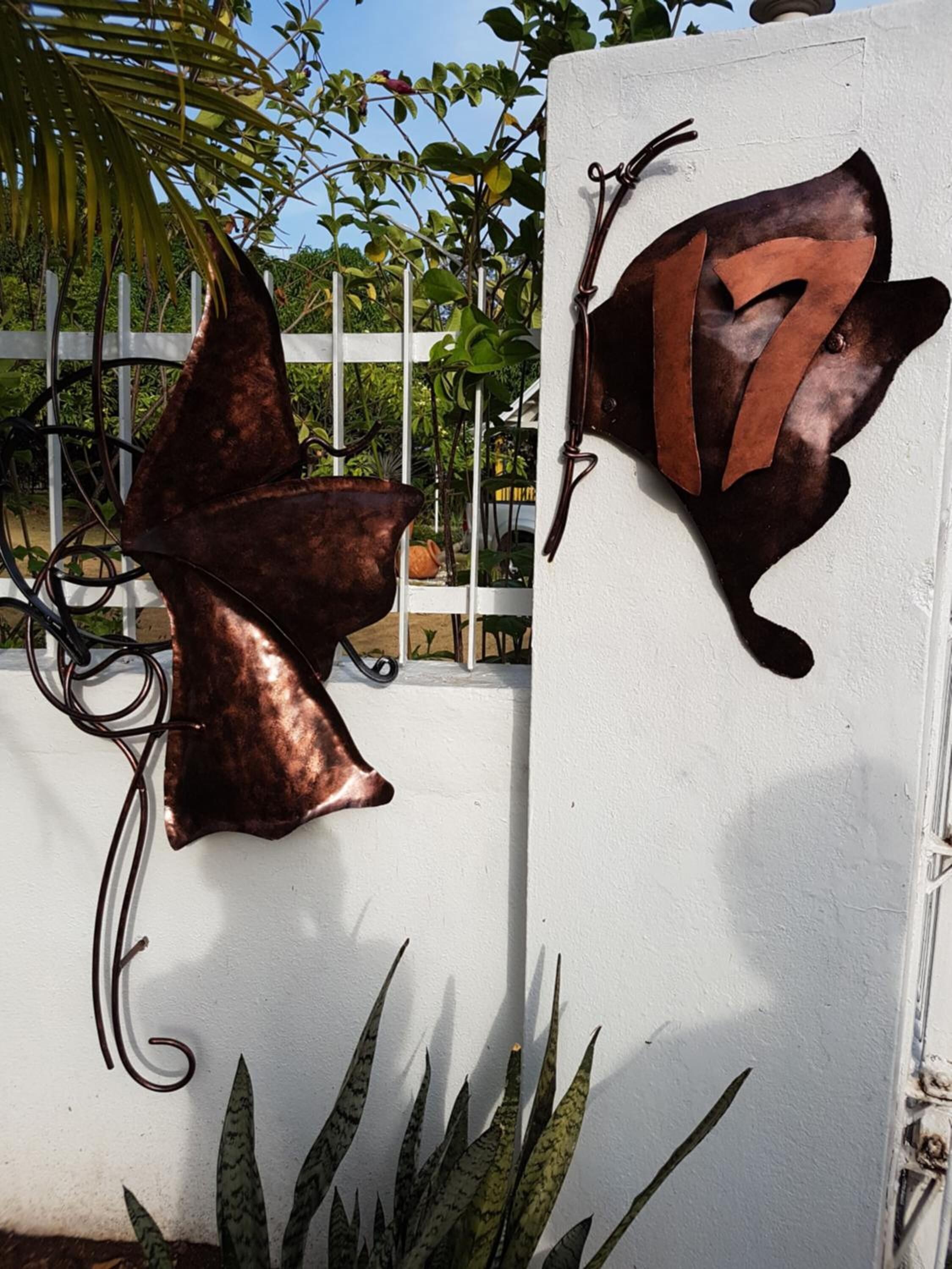 A metal gate with a decorative design, a white wall, and some greenery in the background.
