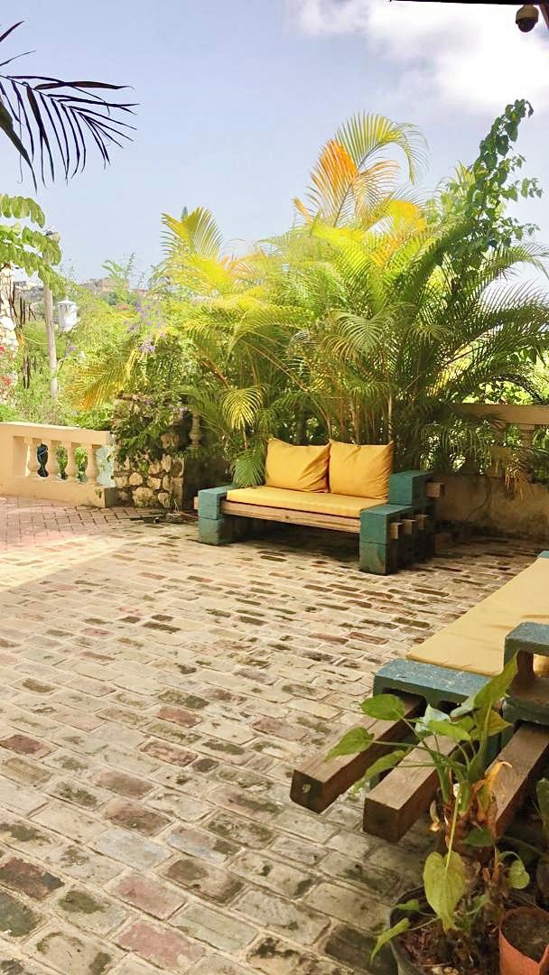 A patio with a stone-tiled floor, a wooden bench, and a sofa with cushions.