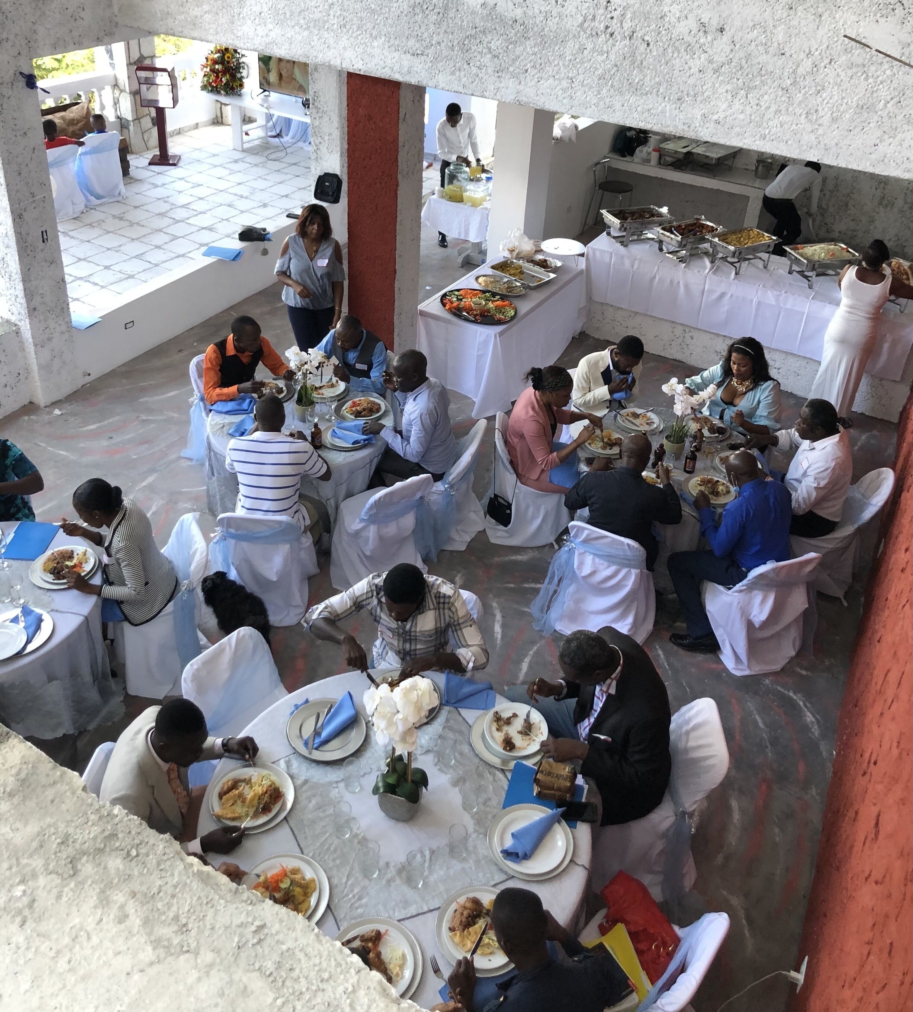 Zona pranzo con tavoli rotondi ricoperti da tovaglie bianche, circondati da sedie bianche.