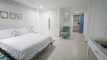 A bedroom with a bed, a nightstand, a chair, and a desk. There is a door leading to a bathroom.