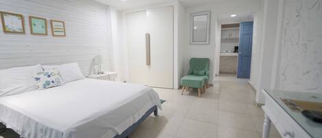 A bedroom with a bed, a nightstand, a chair, and a desk. There is a door leading to a bathroom.