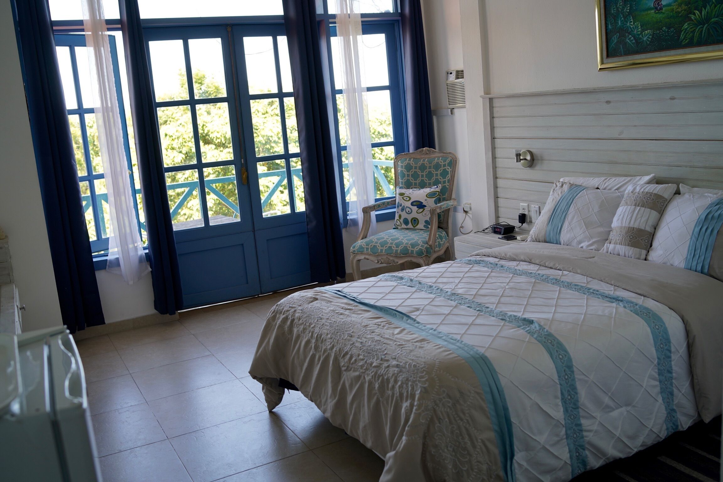 A bedroom with a large bed, a chair, a window with curtains, and a painting on the wall.