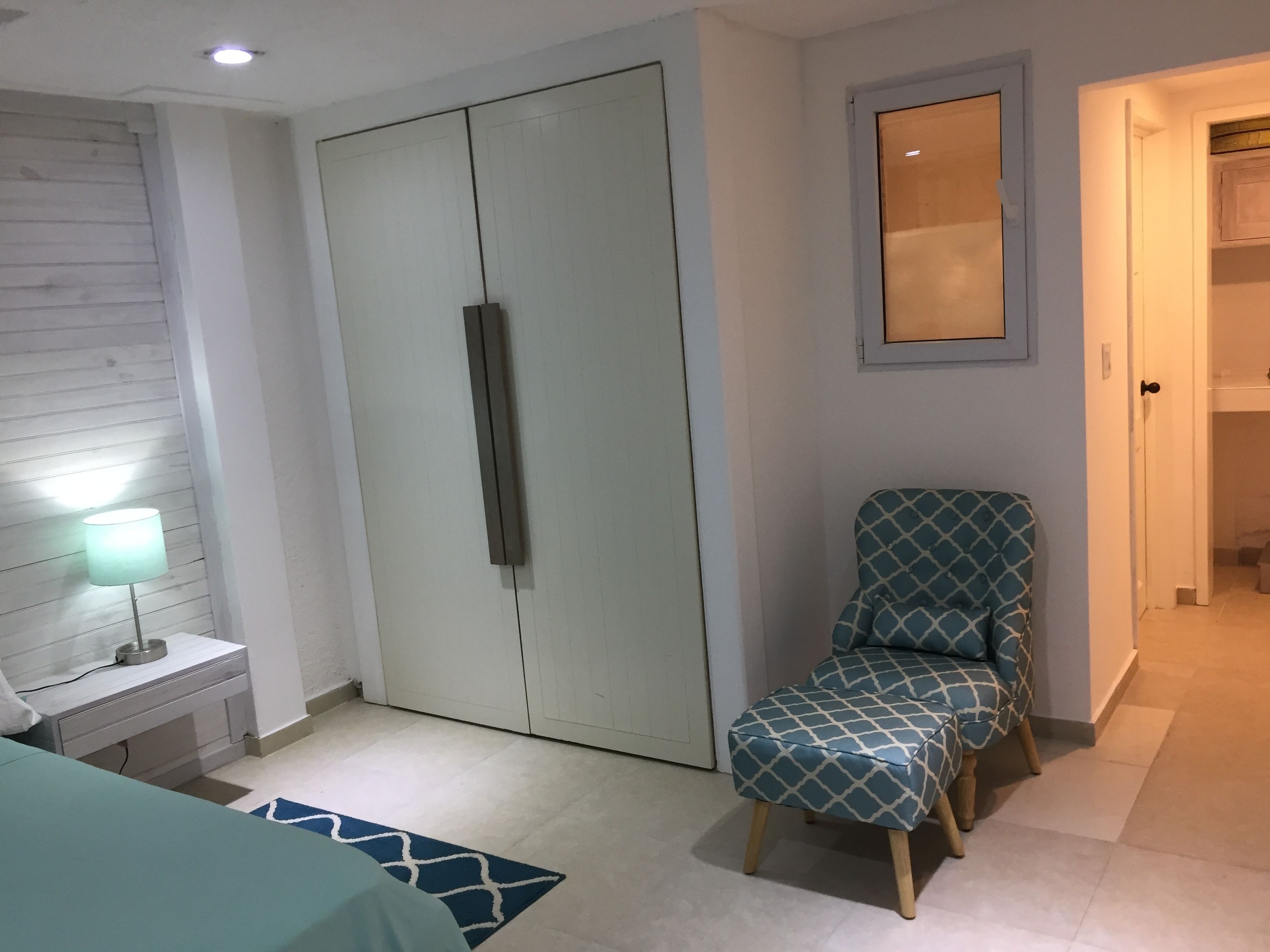 A bedroom with a bed, a nightstand, a lamp, a wardrobe, a chair, and a mirror.
