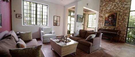 A spacious living room with a piano, a large window, and a stone wall.