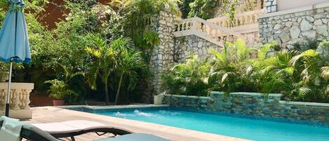 Uma área de piscina com espreguiçadeiras, parede de pedra e vegetação exuberante.