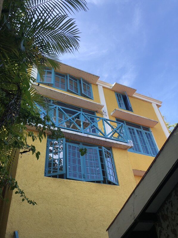 Un edificio de varios pisos con ventanas y balcones de marco azul, paredes amarillas y un cielo azul despejado.