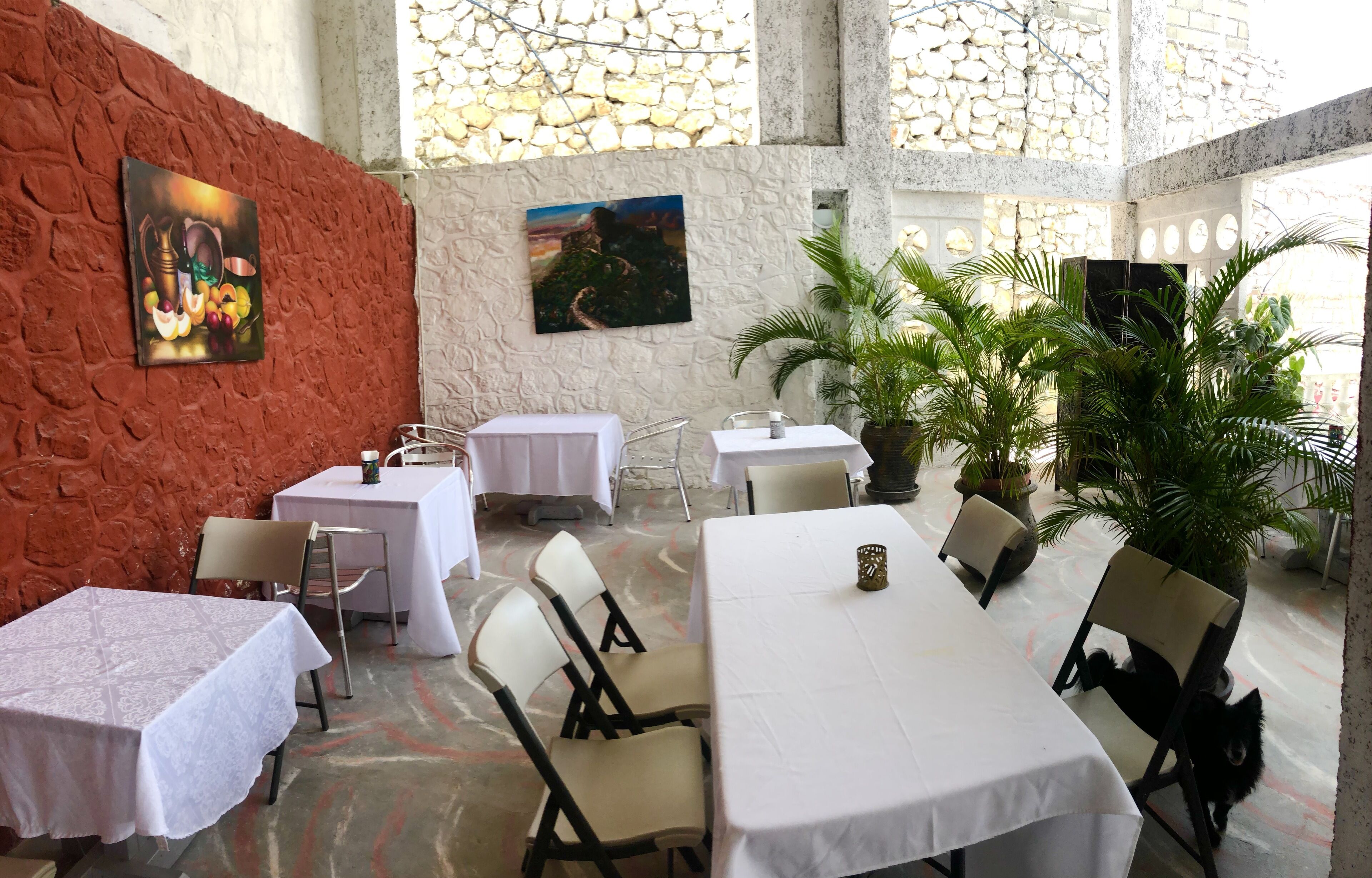 A restaurant with tables and chairs, a stone wall, and potted plants.