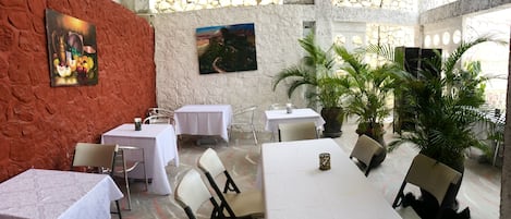 A restaurant with tables and chairs, a stone wall, and potted plants.