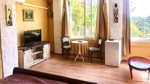 Une chambre avec un lit, une télévision, un petit réfrigérateur, une table avec des chaises et une fenêtre avec des rideaux.