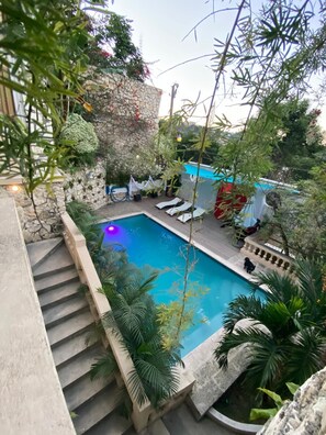 Une piscine bordée d’un muret en pierre et accessible par des marches, entourée de verdure et d’une clôture blanche.