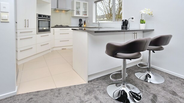 Een moderne keuken met witte kasten, een inbouwoven en een bar met twee krukken.