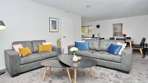 Een moderne woonkamer met twee grijze banken, een zwarte salontafel en een eethoek met een tafel en stoelen.