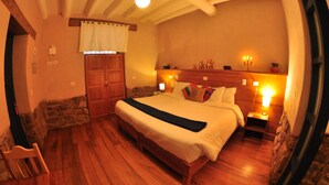A bedroom with a wooden bed, stone walls, a stone fireplace, and a nightstand with a lamp. - Nao Victoria Hostel (Cusco)