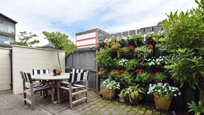 A patio with a wooden table and chairs, surrounded by potted plants and flowers.