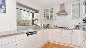 A modern kitchen with white cabinets, a dishwasher, a window with a view, and a stainless steel range hood.