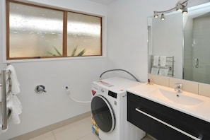 A modern bathroom with a built-in washer and dryer, a large mirror, and a white sink. - Leinster Villa (Christchurch)