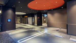 Un hall d’hôtel moderne doté d’une entrée accessible aux personnes en fauteuil roulant, d’un kiosque d’information numérique et d’un grand luminaire rouge.