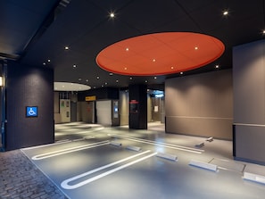 Eine moderne Hotelhalle mit barrierefreiem Eingang, einem digitalen Informationsterminal und einer großen, roten Leuchte.