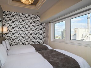 Hotelkamer met behang met patroon, een groot bed met wit en bruin beddengoed, een kroonluchter en een raam met uitzicht op de stad.