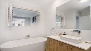 Une salle de bain moderne avec une baignoire sur pieds, un grand miroir et un meuble-lavabo avec un évier et un placard.