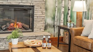 Ein gemütliches Wohnzimmer mit Kamin aus Stein, einem Couchtisch mit Snacks und Bierflaschen, einer bequemen Couch und einer Lampe.