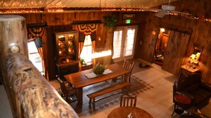 A wooden interior with a dining table, chairs, a bench, a sofa, and a ceiling fan. - The Guest House (Schellsburg)