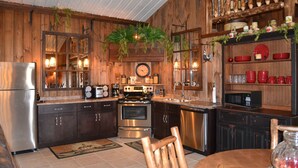 A rustic kitchen with wooden walls, stainless steel appliances, and a clock on the wall. - The Guest House (Schellsburg)