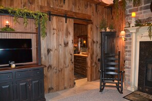 A rustic interior with a wooden wall, a fireplace, a television, and a ladder.
